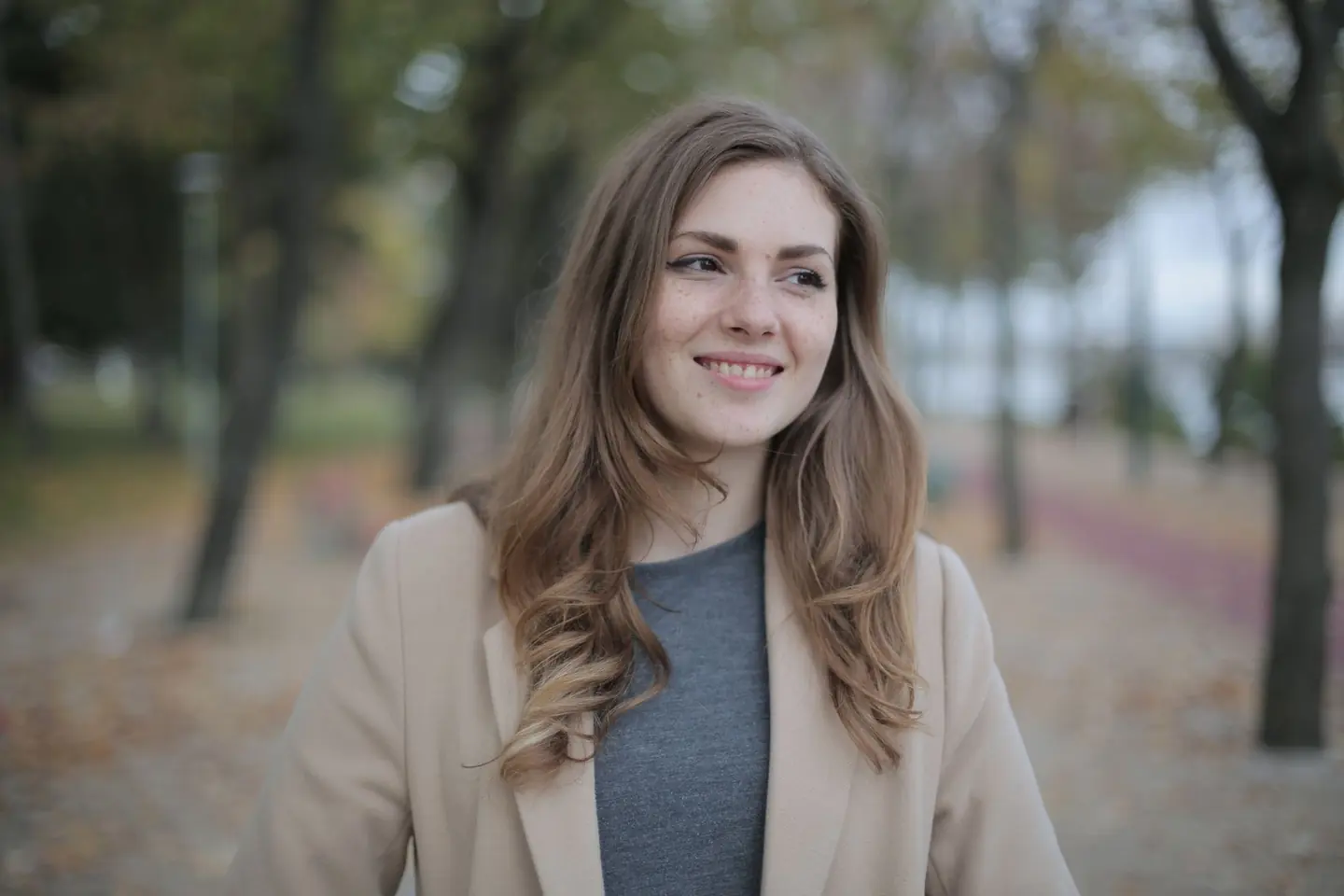 Femke Laan, coach, in een lichte jas tussen de bomen in het park